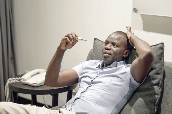 Kranker afrikanischer Mann mit Fieber und Erkältungen schaut ein Thermometer sitti — Stockfoto