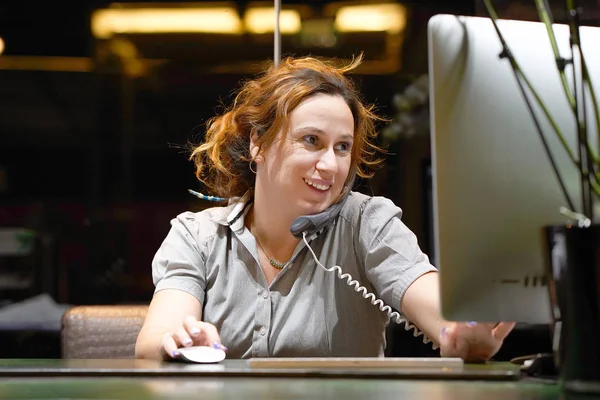 Молода жінка сидить за своїм столом працює і відповідає на телефон — стокове фото