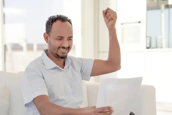 Happy entrepreneur man reading good news in a letter on sofa in