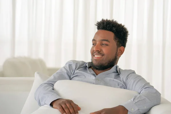 Afričan se usmívá, zatímco sedí na pohovce — Stock fotografie