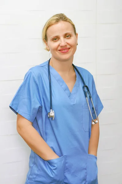 A nurse with blond hair and a stethoscope in uniform is smiling at the camera. — Stock Photo, Image