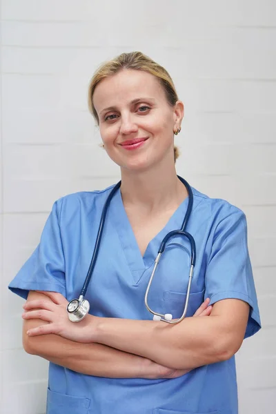 En sjuksköterska med blont hår och ett stetoskop i uniform ler — Stockfoto