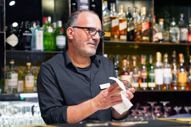 Barmen iş yerinde şarap bardağını siliyor.