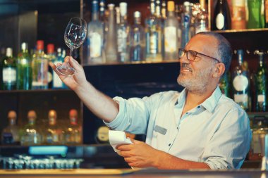 Barmen iş yerinde şarap bardağını siliyor.