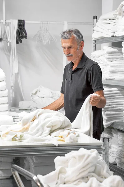 Laundry hotel. A elderly man lays out a white towel. Hotel linen cleaning services.