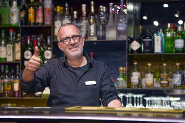 Portrait of elderly Bartender arm show OK. Evening time.