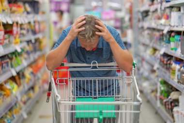 Boş bir alışveriş arabasıyla süpermarkette üzgün bir adam. Krizler, ürün ve ürün fiyatlarının artması. Süpermarkette erkek alışverişi..