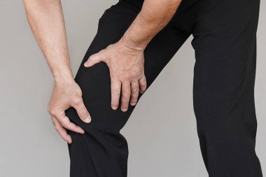 Gri arka planda izole edilmiş ağrılı dizleri olan yaşlı bir erkek bacağı. Yaşlı bir adam eklem ağrısı çekiyor, sağlık sorunları yaşıyor ve elleriyle bacağına dokunuyor. Sağlık hizmeti kavramı.