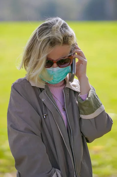 Woman wearing medical mask in street in city and speaks on the phone. Woman walking on the street wearing protective mask as protection against infectious diseases.