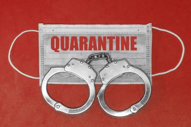 Metin QuarANTINE ile izole tıbbi maske ve kırmızı arka planda kelepçeler. Coronovirus karantina uyum kavramı. Yakından koruyucu maskeler tekstil filtresi.