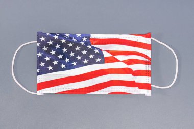 Gri arka planda ABD bayrağı olan izole tıbbi maske. Yakından koruyucu maskeler tekstil filtresi. Sağlık ve tıbbi konsept. Coronavirus, ABD 'de virüs..