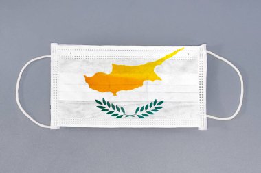 Gri arka planda Kıbrıs bayrağı olan izole tıbbi maske. Yakından koruyucu maskeler tekstil filtresi. Sağlık ve tıbbi konsept. Coronavirus, Kıbrıs 'ta virüs.