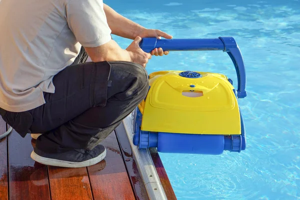 A pool cleaner holds a robot cleaner. Pool cleaner during his work. Caucasian hotel staff worker cleaning the pool