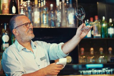 Yakışıklı bir barmen bir bardak şarap bardağını parlatır. Yaşlı barmen bardağı temizliyor. Hizmet kavramı. Arka planda alkol şişeleri olan raflar. Gece vakti..