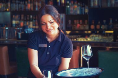 Garson masa servisi yapıyor. Garson, bardaki bir otel restoranında şarap kadehi ve şarap şişesi taşıyor. Hizmet kavramı. Arka planda alkol şişeleri olan raflar. Gece vakti..