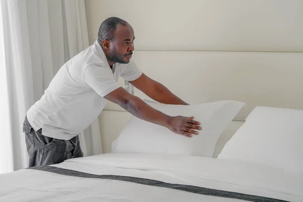 Elderly maid making bed in hotel room. Staff Maid Making Bed. African housekeeper man making bed.