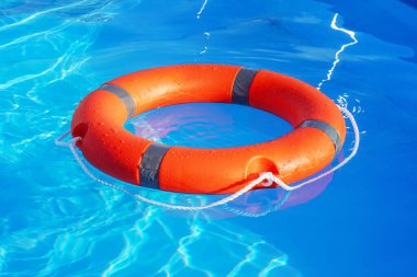 Kırmızı can simidi mavi suda yüzer. Yaşam halkası güneşli mavi suyun üzerinde yüzüyor. Yüzme havuzunda hayat yüzüğü.