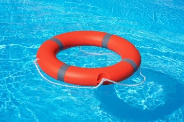 Kırmızı can simidi mavi suda yüzer. Yaşam halkası güneşli mavi suyun üzerinde yüzüyor. Yüzme havuzunda hayat yüzüğü.