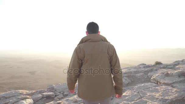 Молодой человек подходит к краю скалы пустыни — стоковое видео