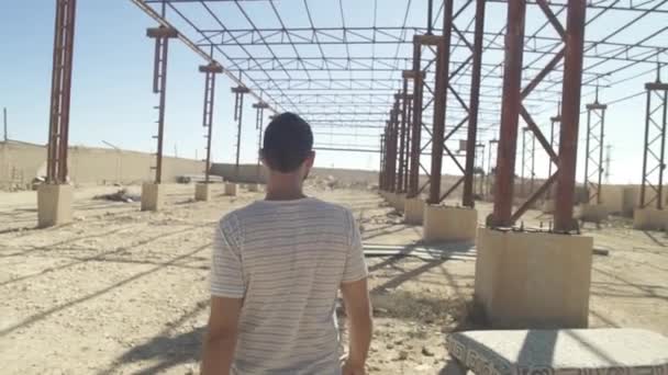 Giovane uomo cammina in una fabbrica fatiscente nel deserto — Video Stock