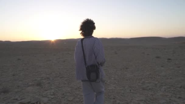 Jovem caminha no deserto com sua câmera — Vídeo de Stock