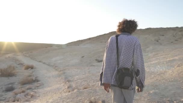 Joven caminando por el desierto con un estuche de cámara — Vídeo de stock