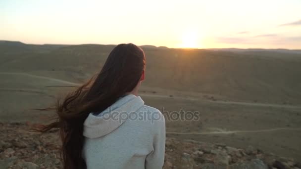 Jovem mulher sentada e olhando para o sol do deserto - câmera empurra dentro — Vídeo de Stock