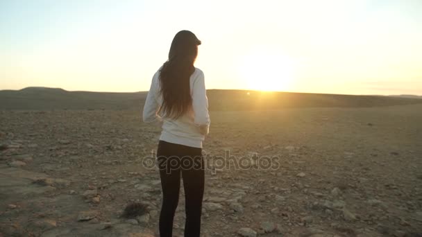 Mujer joven en el desierto mirando al sol — Vídeo de stock