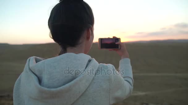 Wanita muda mengambil foto matahari gurun dengan ponselnya. — Stok Video