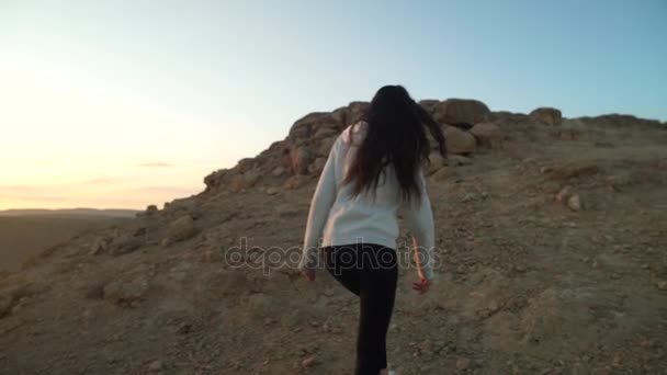 Dospívající dívka lezení pouštními kopci při západu slunce — Stock video