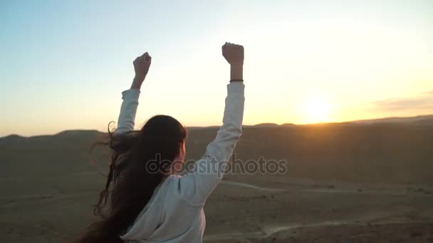 Девушка с поднятыми руками в воздухе на закате пустыни — стоковое видео