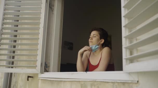 若いです女性に彼女のアパートの窓から彼女のマスクオフと楽しみますザ新鮮な空気 — ストック動画