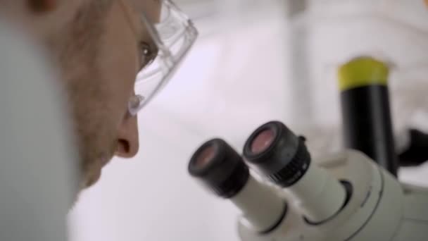 若い科学者は彼の保護メガネを削除し 顕微鏡の中を見る — ストック動画