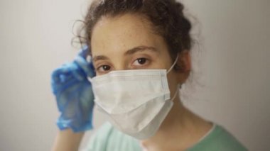 Kadın doktor ya da hemşire, yorgun, maskesini çıkarıyor ve kameraya gülümsüyor.