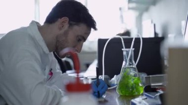 Laboratuvardaki bilim adamı baloncuklu alg şişesine bakarken notlar yazıyor.