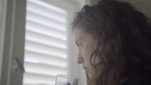 坐在窗边房间里的年轻女人喝着杯子里的水 — 图库视频影像