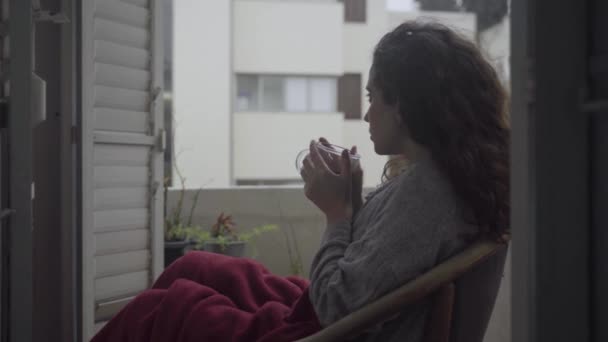 年轻美丽的女人在阳台上坐着 天气很冷 — 图库视频影像