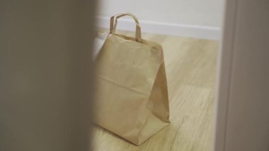 Paket kâğıt torbası koridorda bekliyor, lateks eldivenli kişi topluyor.