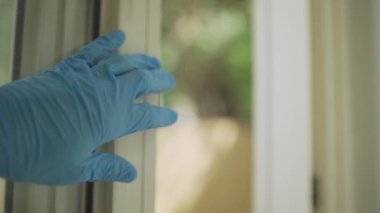 Elindeki lateks eldivenle pencereye uzanır ve kapatır.