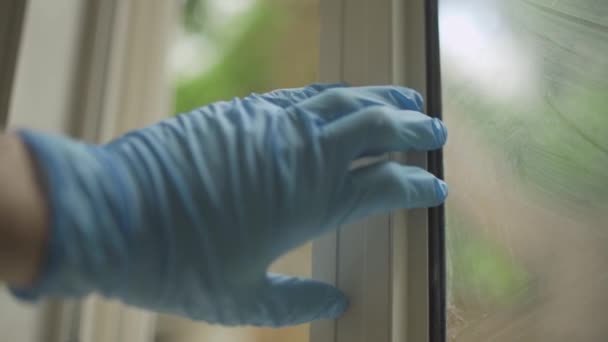 Ruka s modrou latexovou rukavicí zavírající okno nebo skleněné dveře v domě nebo bytě
