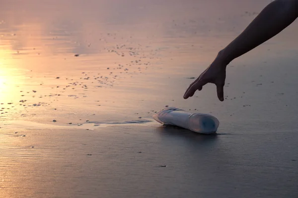 En kvinnes hånd plukker opp en plastflaske – stockfoto