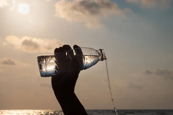 Ręka jest nalewanie wody z butelki na plaży na nawetw — Zdjęcie stockowe