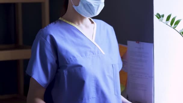 Person in medical mask and uniform slowly picks up piece of paper that says "you will all die" and laughs. Crazy joke during coronavirus outbreak. Nurse showing "you will all die" sheet and laughing. — Stock Video