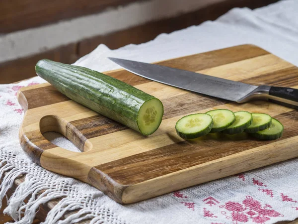 Свежий зеленый огурец нарезанный на ломтики ножом на деревянном кабане — стоковое фото