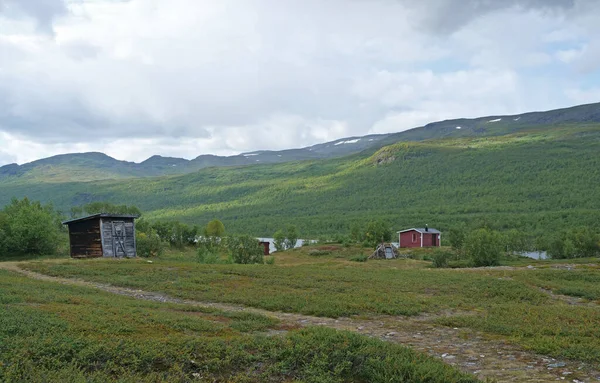 Case Sami nel verde paesaggio collinare del Parco Nazionale di Abisko. Goahti è un'abitazione tradizionale lappona realizzata in tessuto, muschio di torba e legno. Lapponia, Svezia settentrionale sul sentiero Kungsleden. Estate soleggiata — Foto Stock