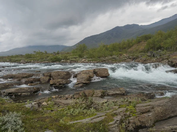 野生Tjaktjajakka河瀑布瀑布瀑布瀑布，桦树森林和山脉。 夏天的拉普兰自然景观，多愁善感的天空. — 图库照片