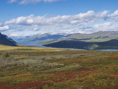 Lulealven nehri ile Laponya manzarası, İsveç 'in Saltoluokta yakınlarındaki Kungsleden yürüyüş parkurunda karla kaplı dağ. Sonbahar renkli çalıları, huş ağaçları ve çalıları olan vahşi doğa. Mavi gökyüzü beyaz bulutlar.