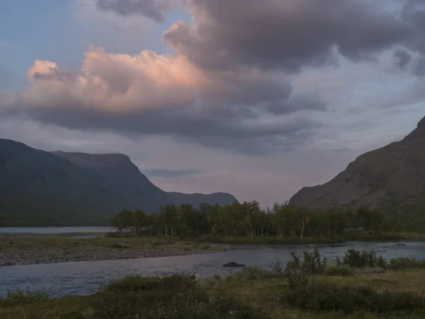 Confluência do rio Tjaktjajakka selvagem e lago Kaitumjaure com pequena ilha de floresta de bétula e montanhas. Lapland paisagem natureza no verão, pôr do sol nuvens rosa — Fotografia de Stock