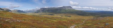İsveç Laponya 'daki Sarek Ulusal Parkı' nda kar kaplı dağ zirveleri, nehir ve göl, huş ağacı ve ladin ağaçlarıyla panoramik manzara. Sonbaharın ilk renkleri, mavi gökyüzü beyaz bulutlar.