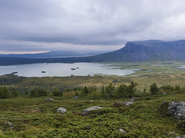 Pohled na klikatící se říční deltu v údolí Rapadalen v národním parku Sarek ve Švédsku. Laponské hory, skály a břízy. Brzké podzimní barvy, náladová obloha s mraky. — Stock fotografie